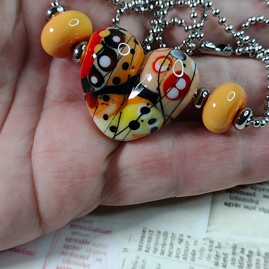 Short video of tan and orange patchwork heart necklace in hand for scale 